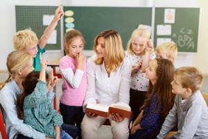 Eine Lehrerin ist umringt von Kindern und liest aus einem Buch vor.