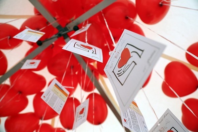Herzförmige rote Luftballons, an denen Postkarten mit dem Logo der Initiative Organspende und Spenderausweise hängen