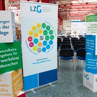 Große Pappwürfel sind aufgestapelt neben einem Rollup. Alles beschriftet mit Projekten der LZG.