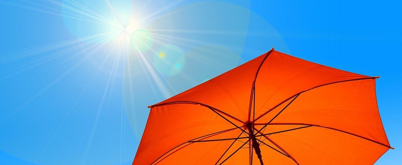 Ausschnitt eines roten Sonnenschirms vor einem blauen Himmel mit Sonne.