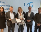 Zwei Frauen und drei Männer präsentieren eine aufgeschlagene Dokumentenmappe.