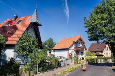 Eine Frau spaziert auf einer Straße mit alten Häusern und grünen Vorgärten