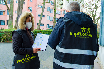 Eine Impflotsin und ein Impflotse stehen in einem Wohngebiet.