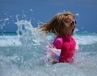 Ein Mädchen mit Sonnenschutzkleidung und Sonnenbrille springt im Meer umher.