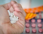 Eine Hand hält mehrere Tabletten, im Hintergrund sieht man unscharf weitere Tabletten.